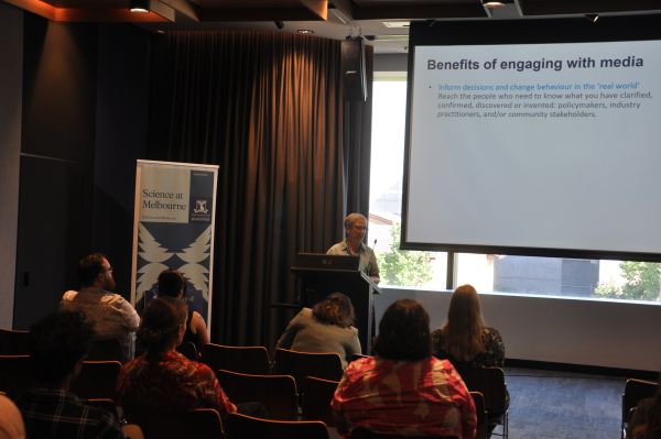 A speaker at the podium next to a slide titled 'Benefits of engaging with media'