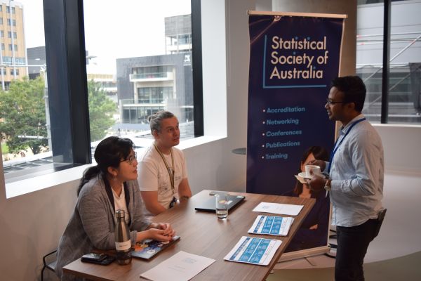 A conference attendee speaking to two people staffing the 'Statistical Society of Australia' booth