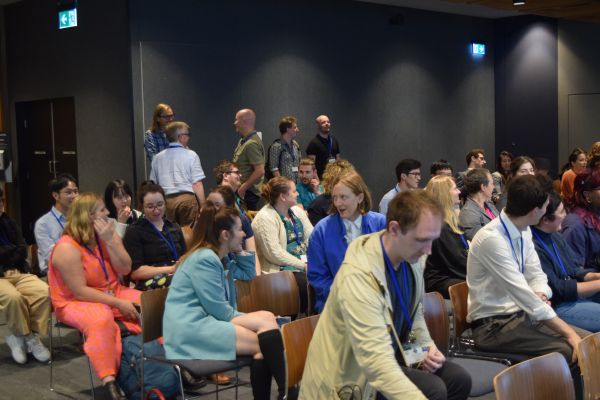 A wide-angle shot of audience members (mostly but not all seated) talking