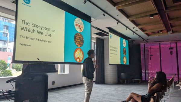 A speaker in front of slides with the title 'The Ecosystem in Which We Live'