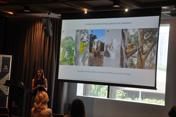 A speaker at the podium, next to a slide titled 'Consider alternative methods, materials and 'stakeholders''