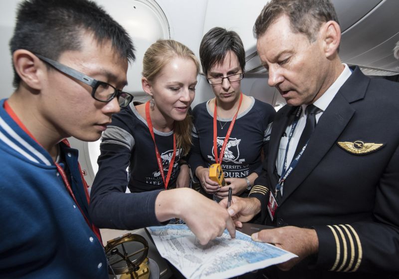 A group of four people looking at a map of Antarctica on on aeroplane